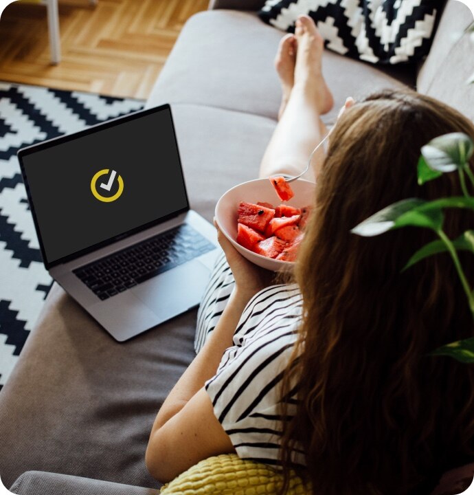 女子在沙发上一边吃西瓜，一边用笔记本电脑启动 Norton 360 AntiVirus 增强版